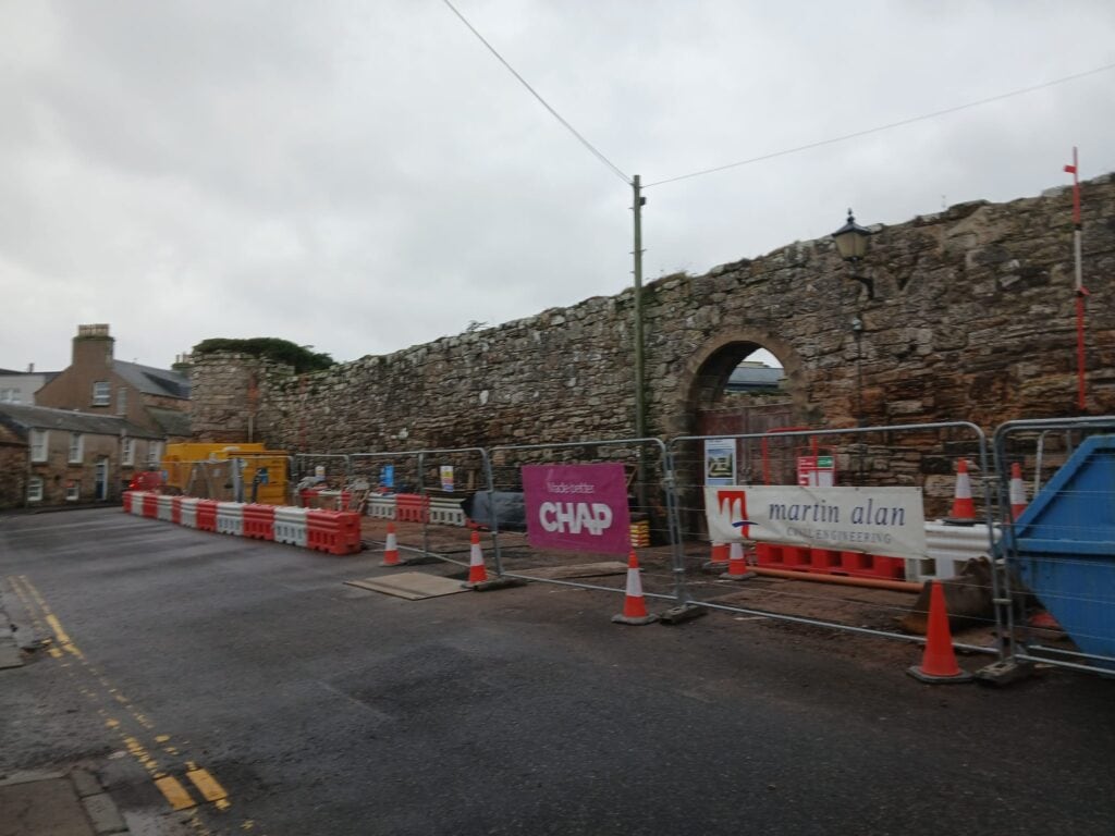 Construction site at St Andrews with historic stone wall and safety barriers.