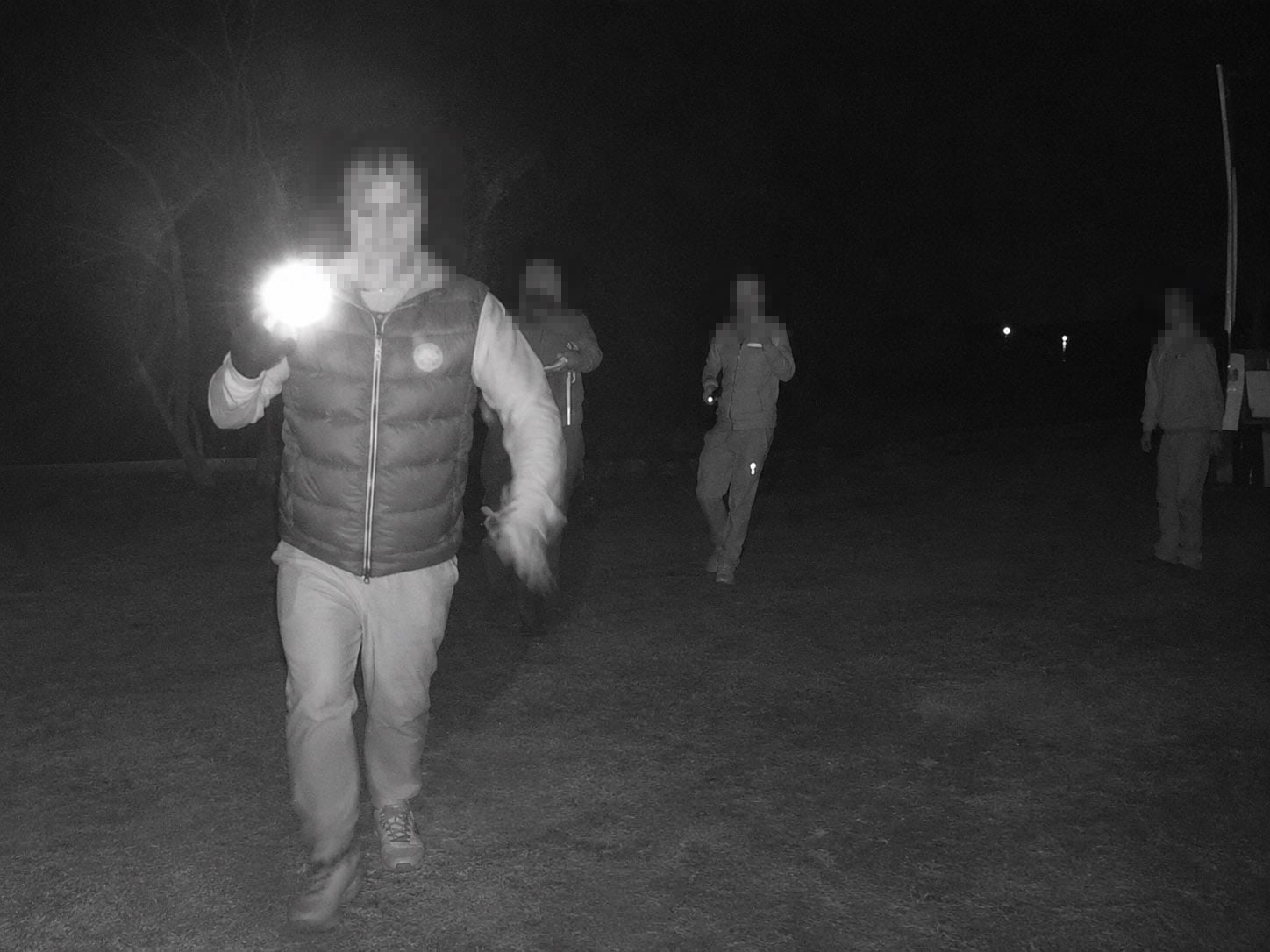 Security personnel patrolling at night with flashlights in an open area.
