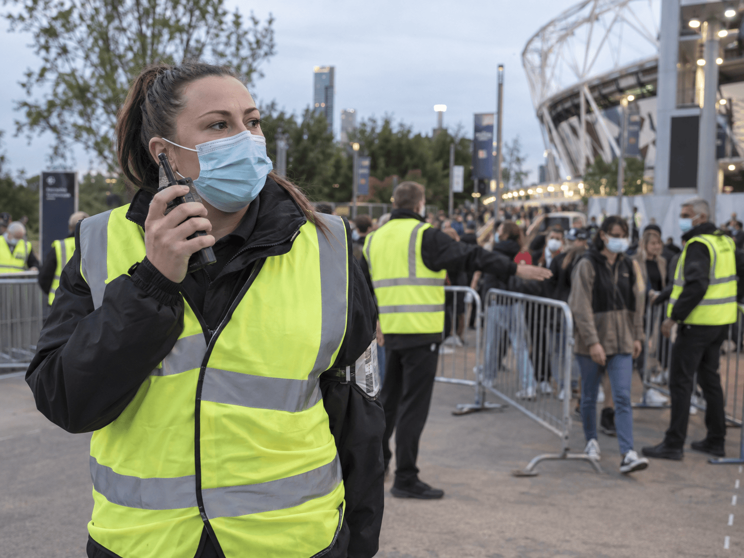 Security personnel wearing high-visibility jackets and face masks at event entrance.