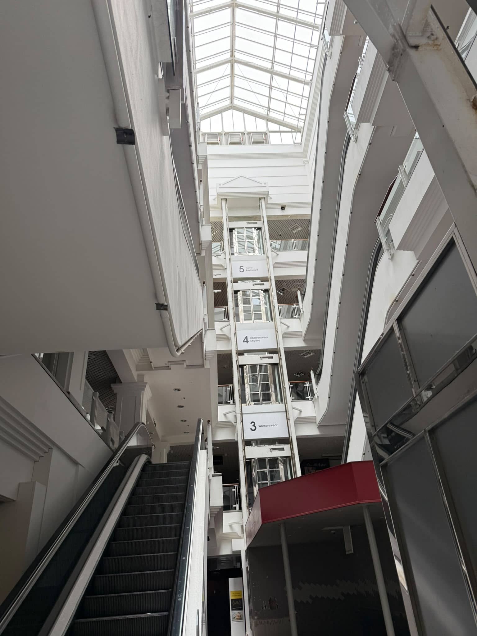 Interior view of a shopping mall with escalators and glass roof.